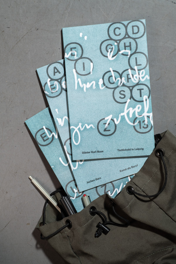 Ansicht von oben auf die Öffnung eines Rucksacks, aus dem mehrere blaue Bücher aufgefächert herausschauen.